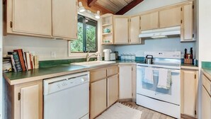 Eine Küche mit Holzschränken, einem Geschirrspüler, einem Backofen und einem Fenster, das für natürliches Licht sorgt.