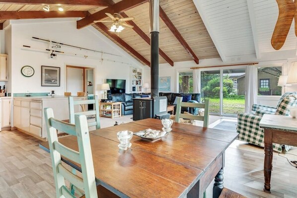 Een ruime woonkamer met een houten eettafel, een bank en een groot raam met uitzicht op het omliggende landschap.