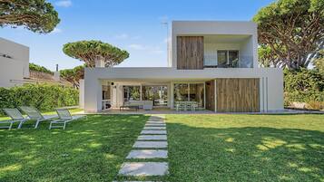 Een modern huis met twee verdiepingen, een overdekt terras, buitenzitplaatsen en een keurig onderhouden gazon.