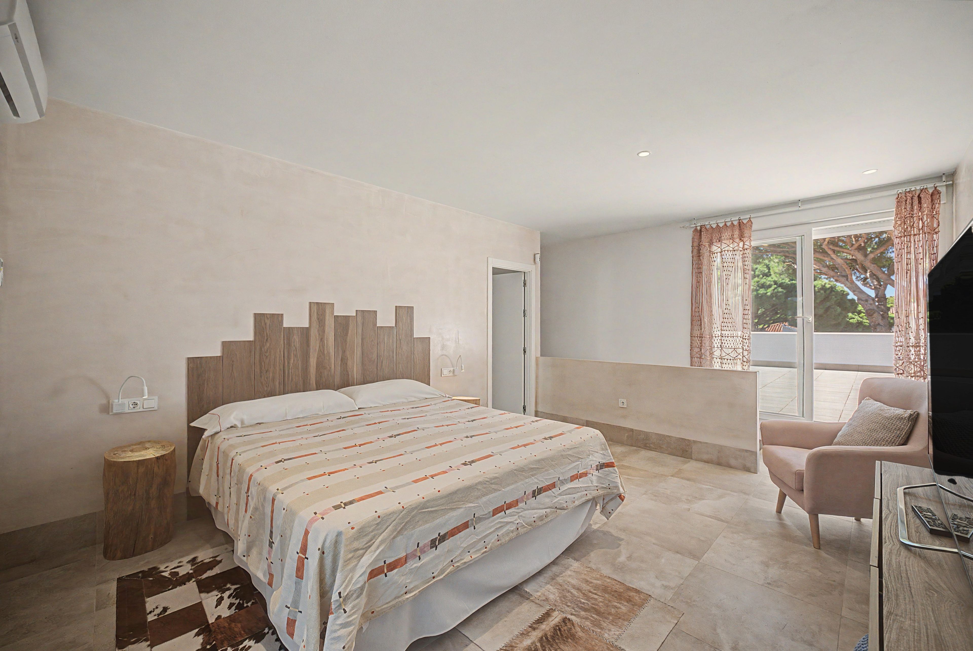 A bedroom with a bed, bedside table, chair, and a window with curtains.