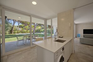A modern kitchen with a built-in washing machine, large windows, and a view of a garden.