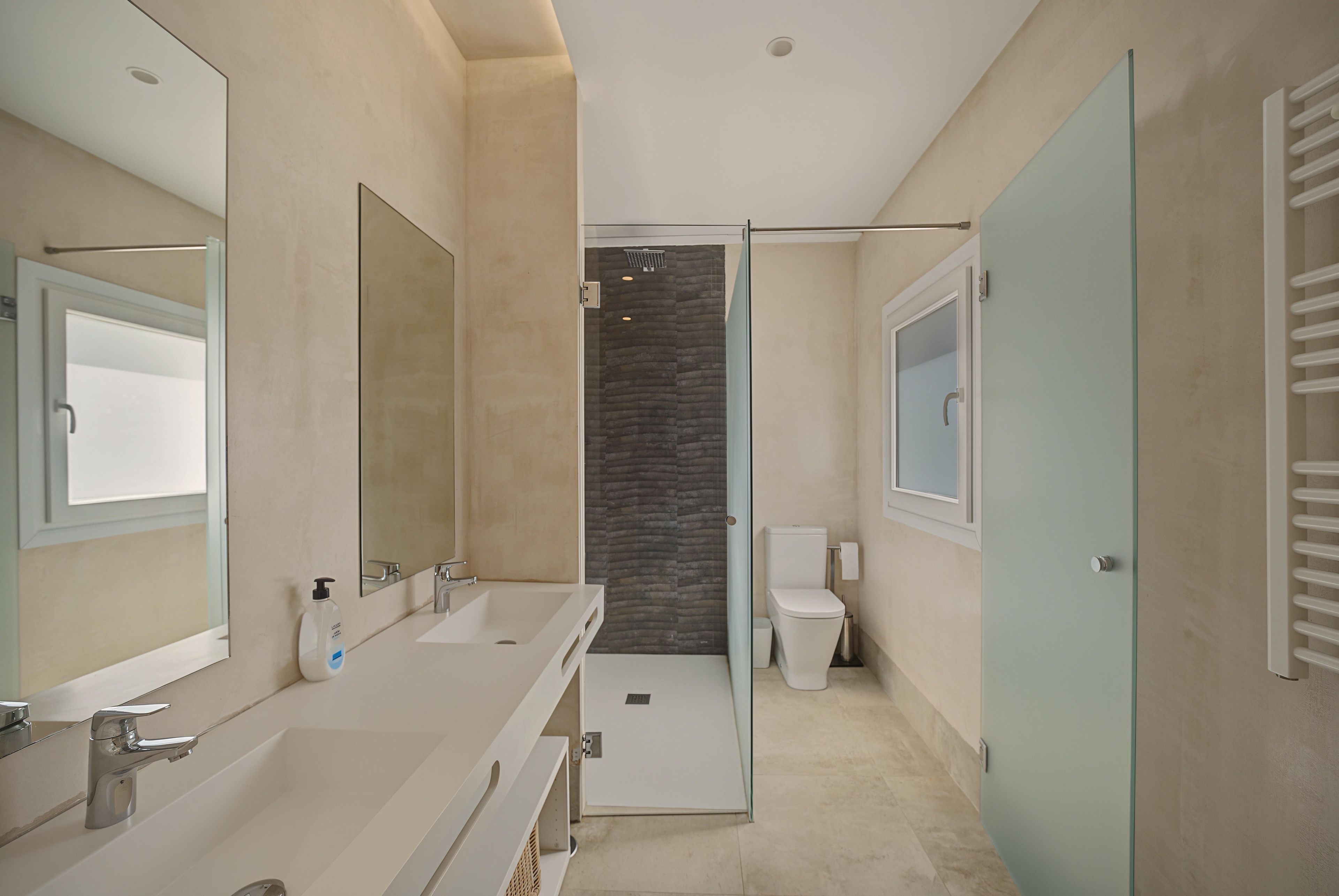 Un baño moderno con mampara de vidrio, inodoro blanco y tocador con espejo.