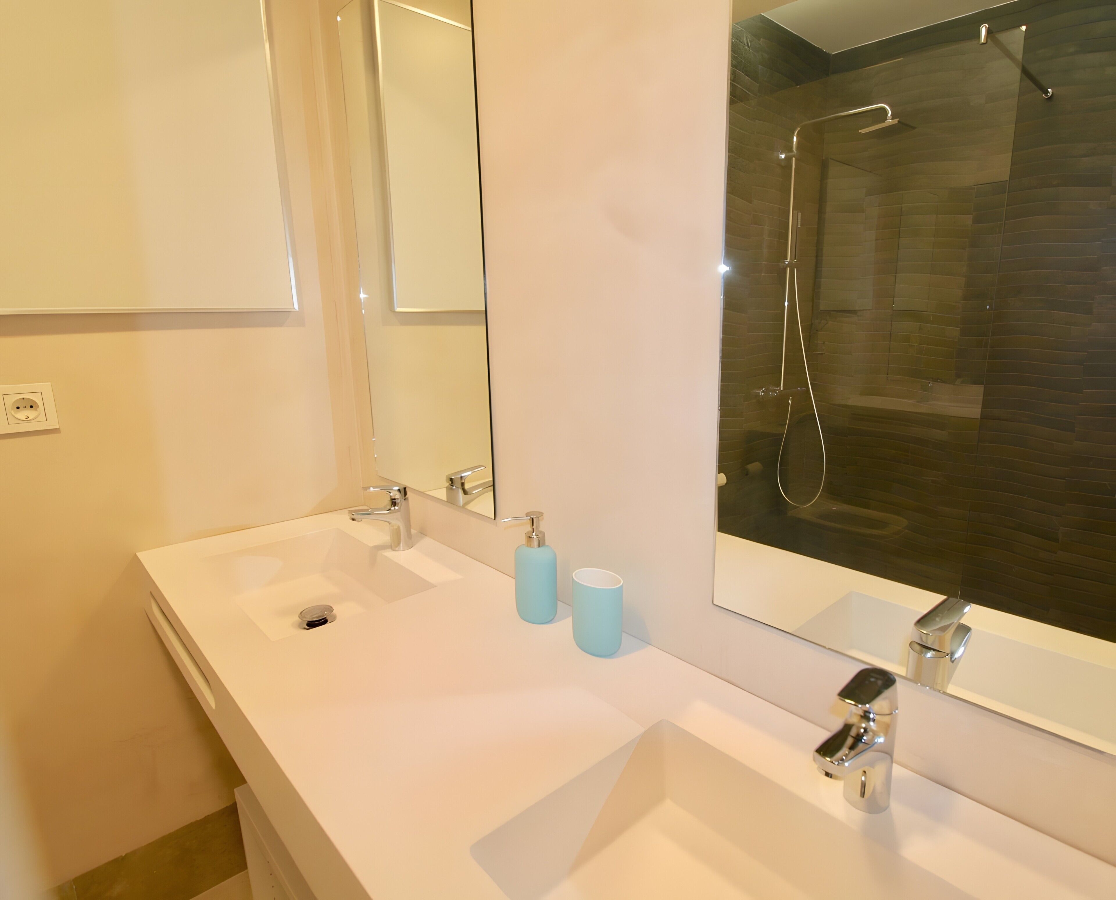 A bathroom with a double sink, a mirror, a shower, and a toilet.