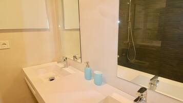 A bathroom with a double sink, a mirror, a shower, and a toilet.