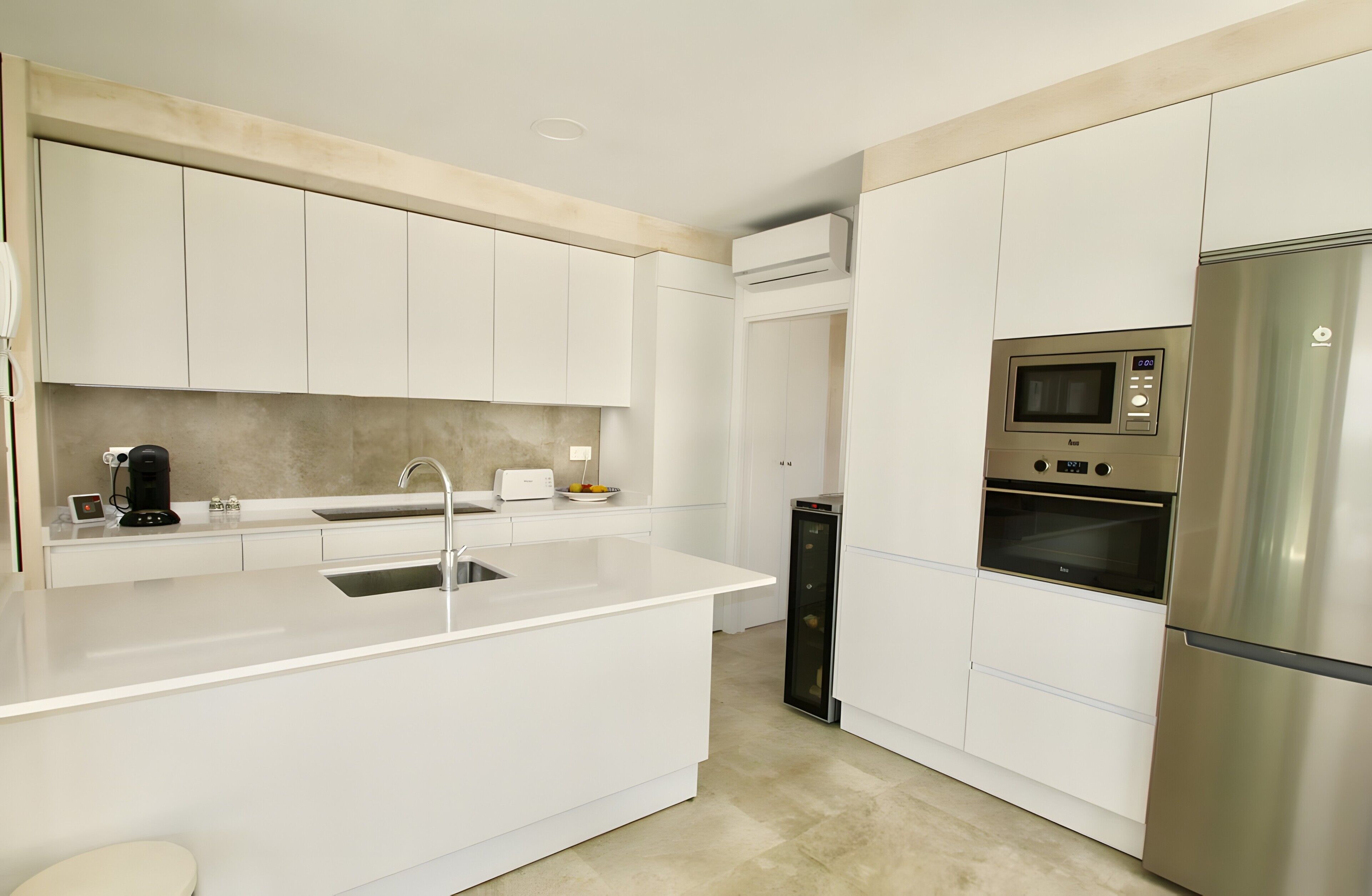 A modern kitchen with white cabinetry, a stainless steel refrigerator, a built-in microwave, and a coffee maker.