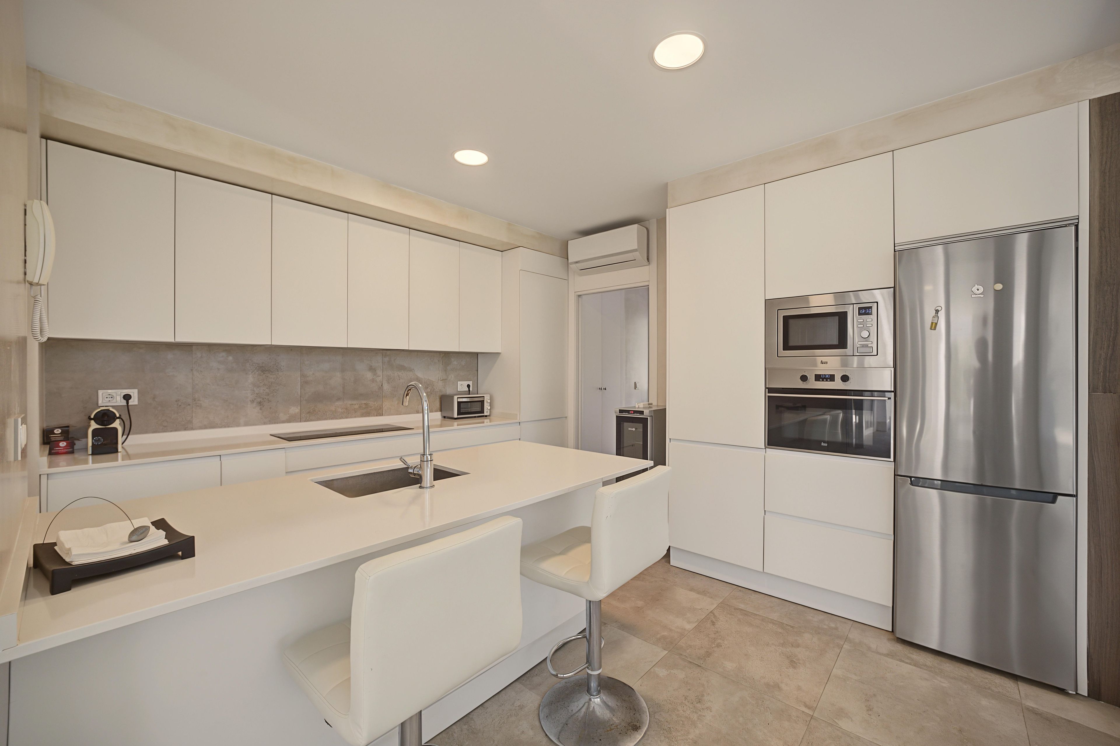 A modern kitchen with white cabinetry, a stainless steel refrigerator, a built-in oven, and a microwave.