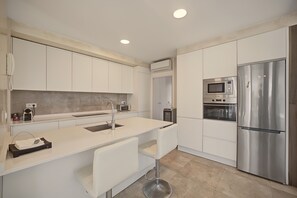 A modern kitchen with white cabinetry, a stainless steel refrigerator, a built-in oven, and a microwave.