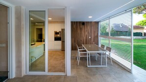 A modern kitchen with a built-in oven and microwave, a dining area with a table and chairs, and a view of a green garden through large windows. - Villa Playa de Roche: private pool, 1000m² garden, 2 en suite bathrooms (Roche)