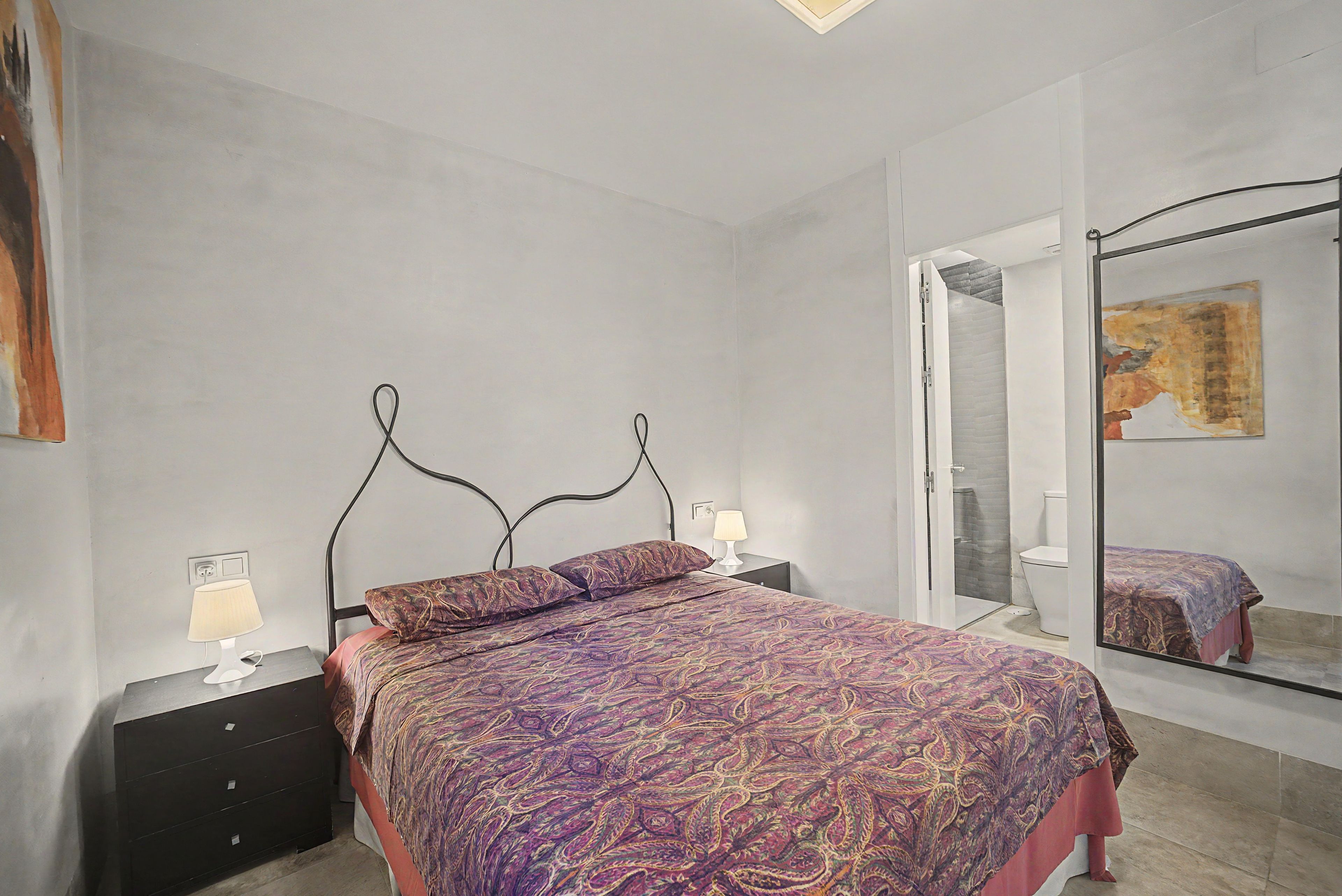 Een slaapkamer met een bed, nachtkastjes, een spiegel en een badkamer die door een geopende deur zichtbaar is.