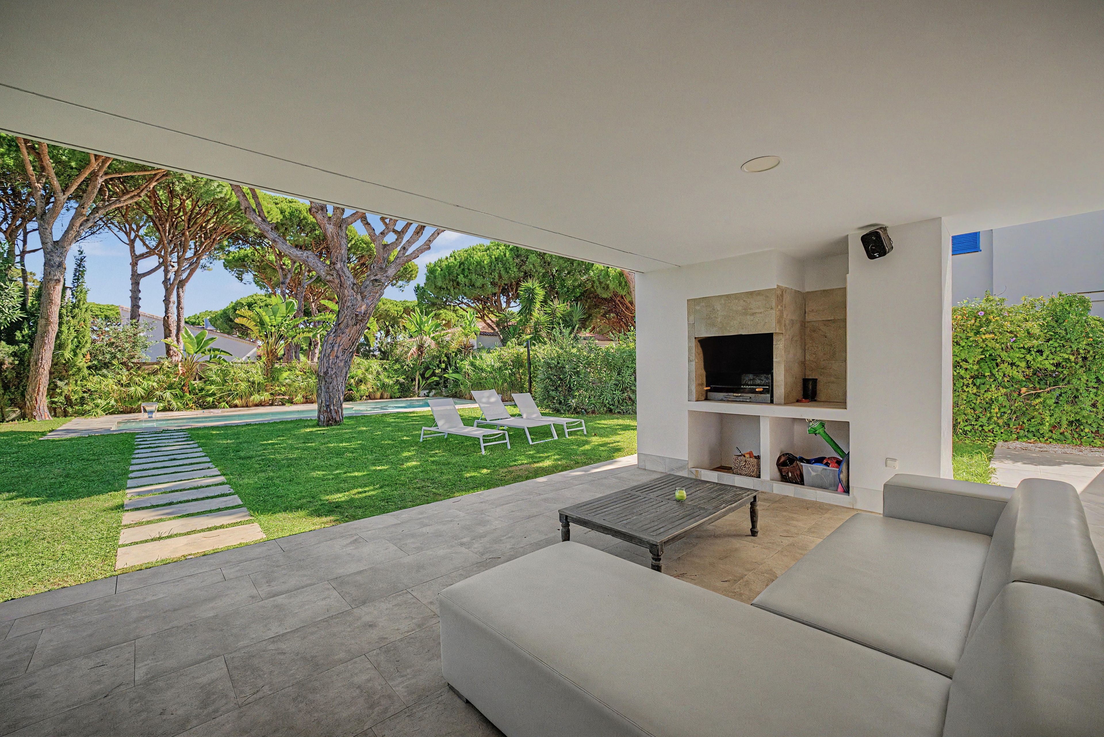 A modern outdoor living area with a sofa, a coffee table, and a TV mounted on a wall.