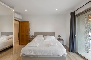 Un dormitorio moderno con una cama grande, puerta de madera y vistas a través de un ventanal.