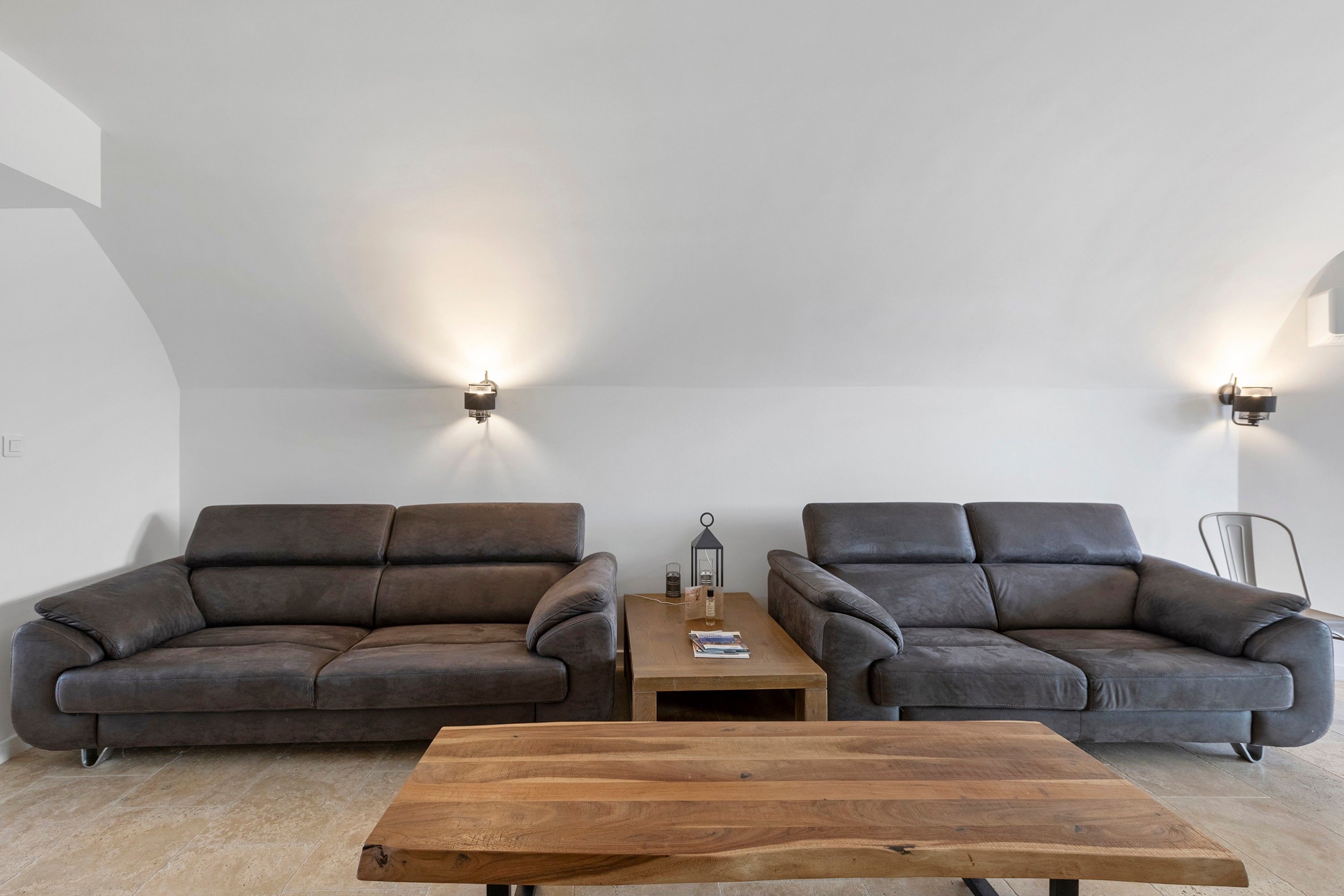 Ein modernes Wohnzimmer mit zwei dunklen Sofas, einem Holztisch und Wandleuchten.