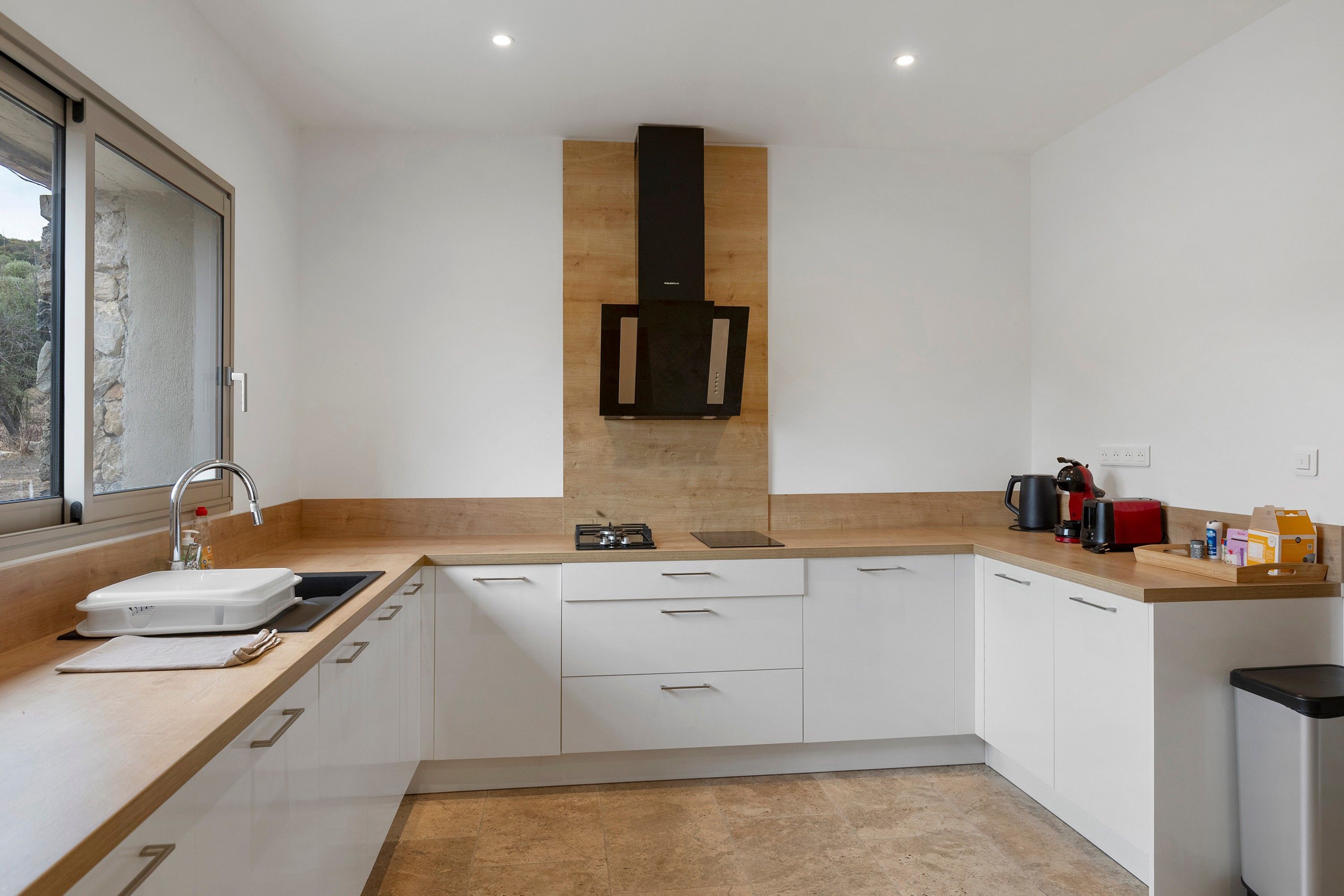 Eine moderne Küche mit weißen Schränken, einer Holz Arbeitsplatte, einem eingebauten Herd und einem Fenster.