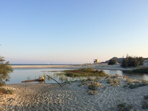 A beach with a lifeguard tower, calm water, and sparse vegetation.