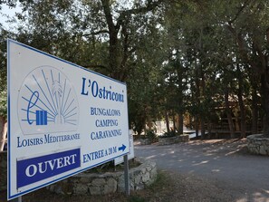 A sign for L'Ostriconi offering bungalows, camping, caravanning, and leisure Mediterranean activities.