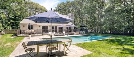 A backyard with a swimming pool, patio furniture, and a covered seating area.