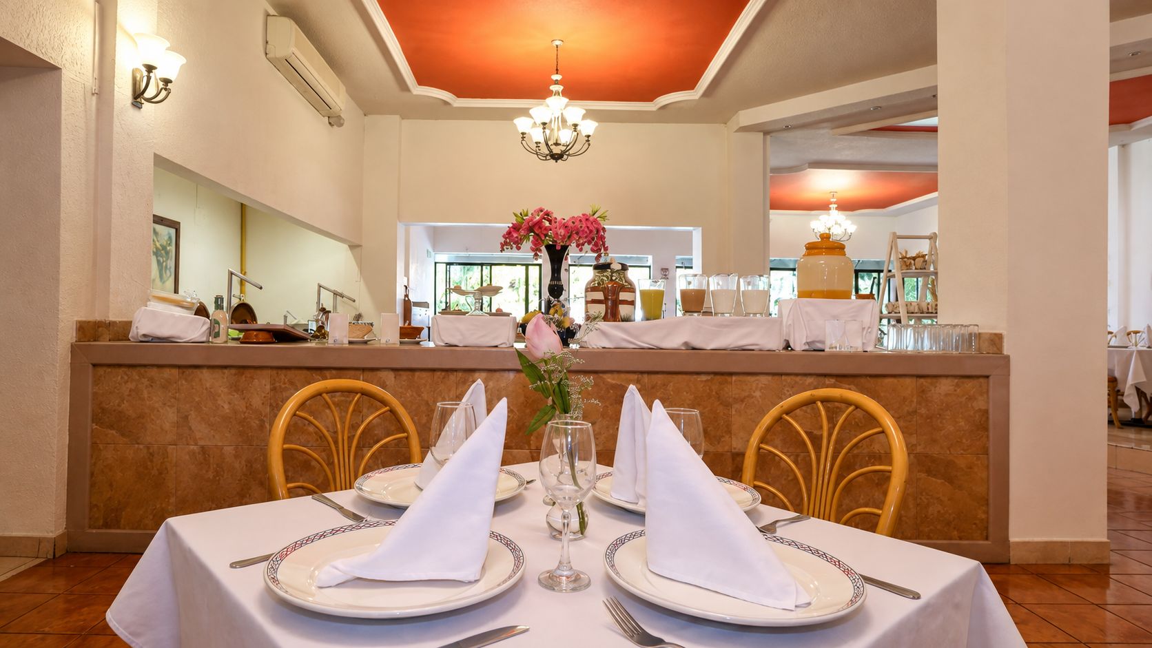 Un comedor con una mesa dispuesta para dos, un florero con flores y una barra en el fondo.