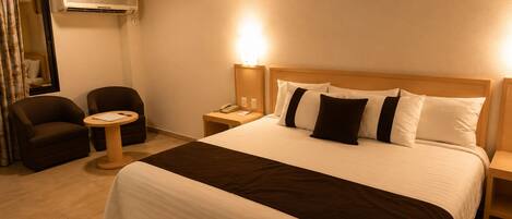 A hotel room with a large bed, a bedside table, a chair, and a small round table.