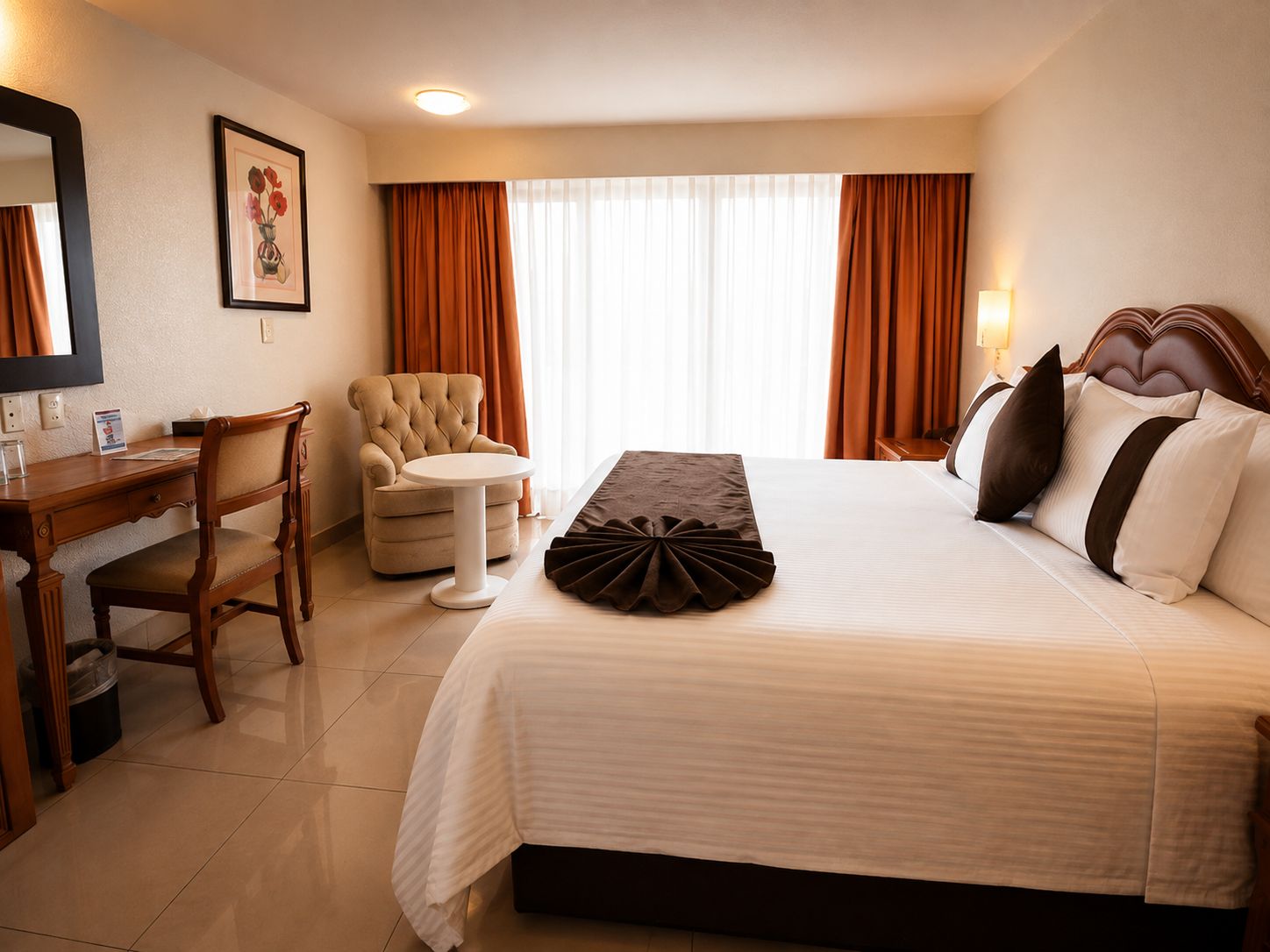 Habitación de hotel con cama, escritorio, silla, mesita y ventana con cortinas.