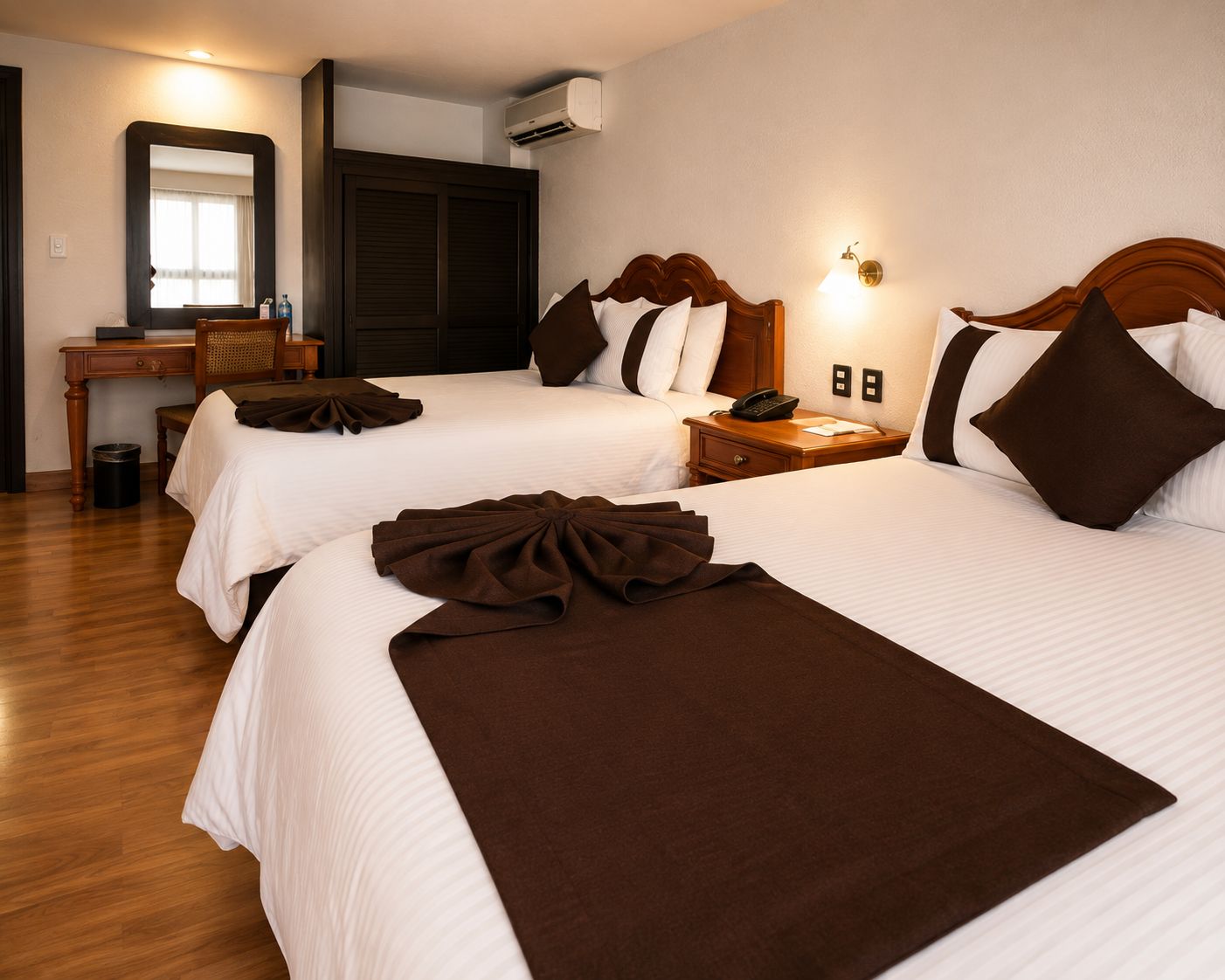 Habitación de hotel con dos camas, un escritorio, un espejo y un equipo de aire acondicionado.