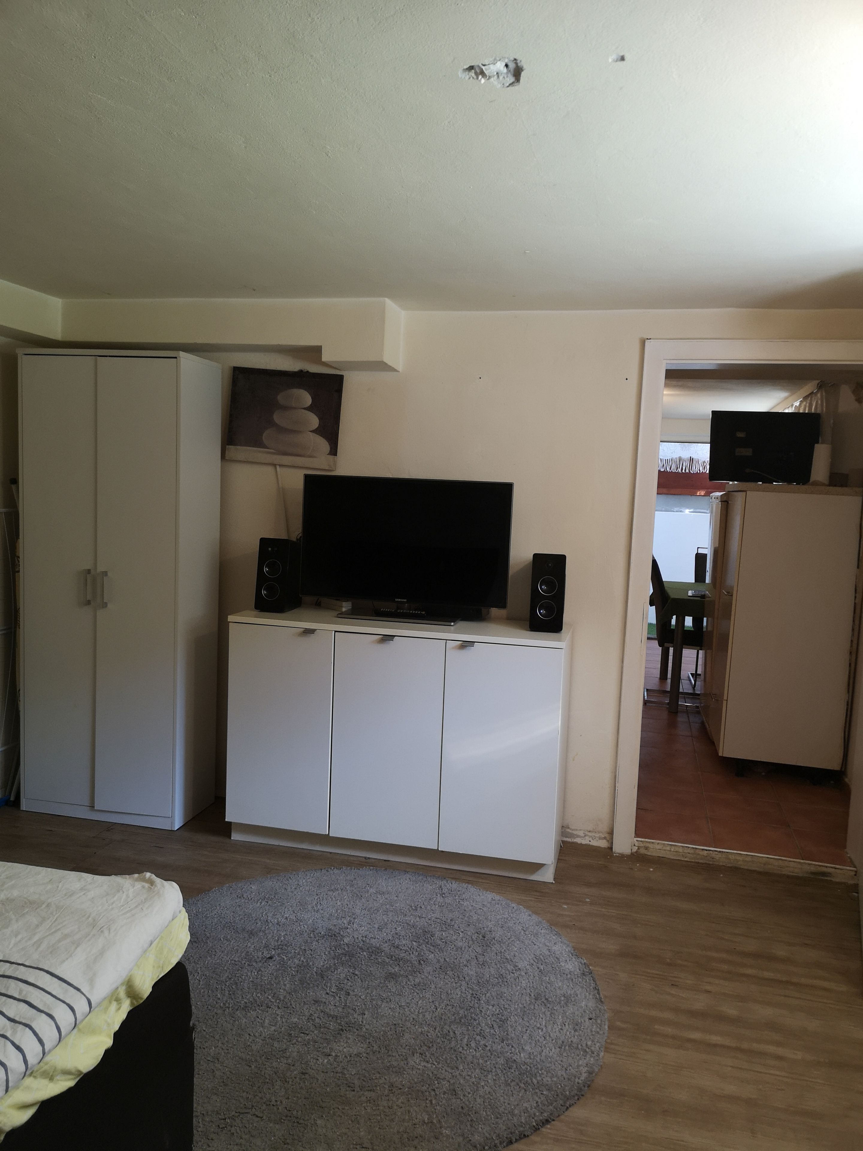 Ein Zimmer mit Fernseher auf einem Schrank, einem Bett mit gestreifter Decke und einem grauen Teppich.