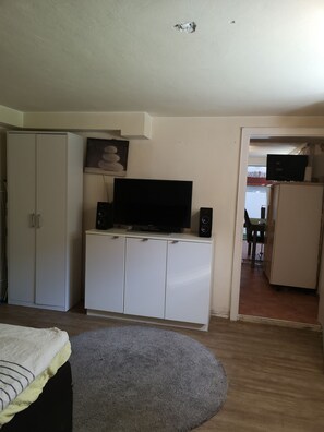 A room with a television on a cabinet, a bed with a striped blanket, and a grey rug.