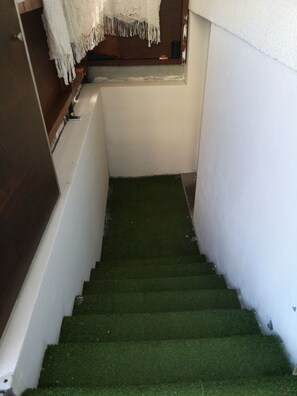 A narrow stairway with green carpeted steps leading to a landing.