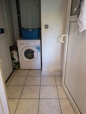 A laundry room with a washing machine, a blue basket, and a white cabinet.