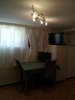 A dining area with a table, chairs, a television on a cabinet, and a ceiling light fixture.