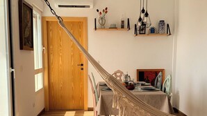 Una habitación con piso de madera, una mesa de comedor con sillas, una hamaca y una puerta de madera.
