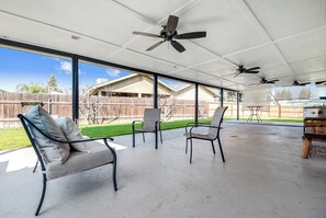 A covered patio area with ceiling fans, outdoor furniture, and a view of a backyard.