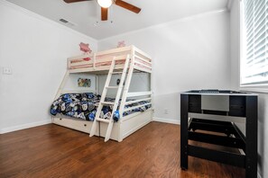 Une chambre avec un lit superposé, un bureau et un ventilateur de plafond.