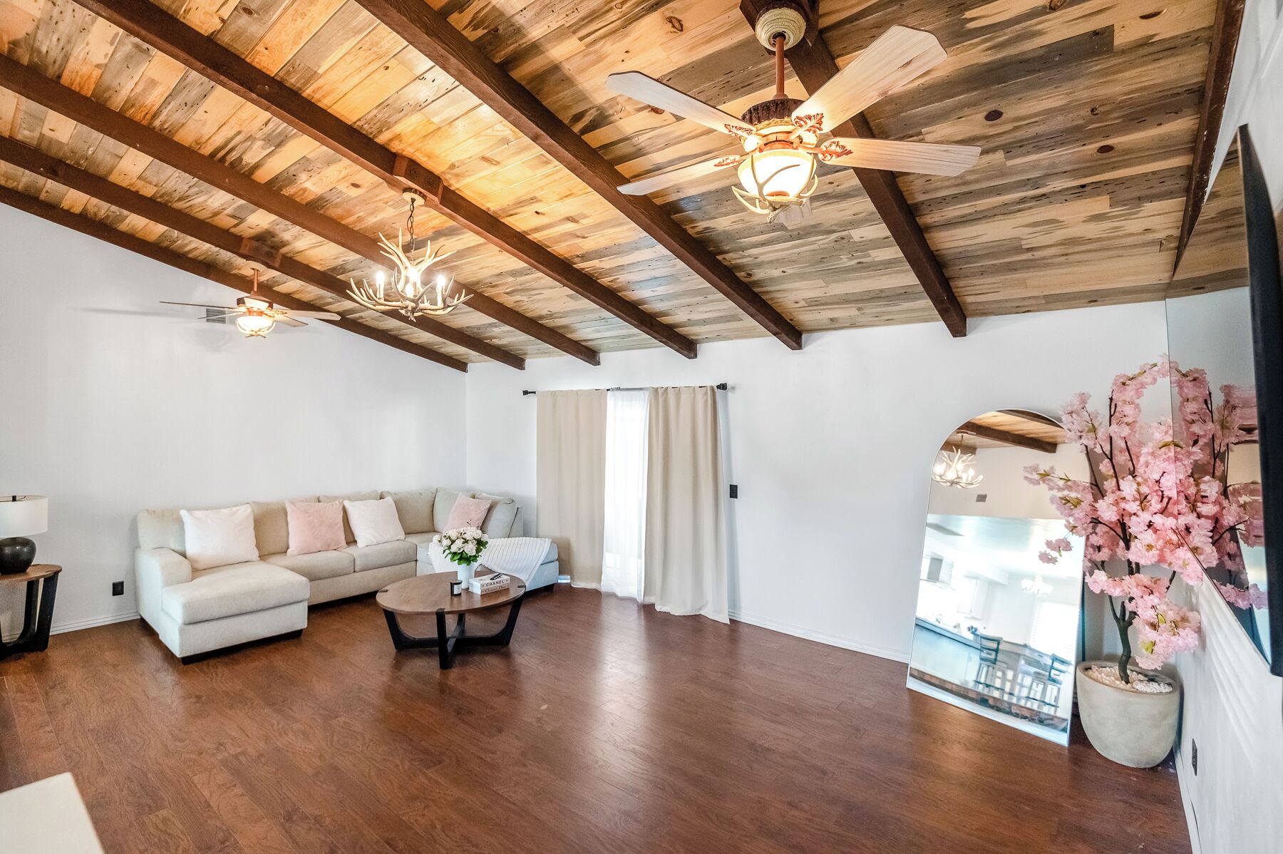 Un salon spacieux avec un plafond haut, des poutres apparentes, un canapé, une table basse et une grande fenêtre avec des rideaux.