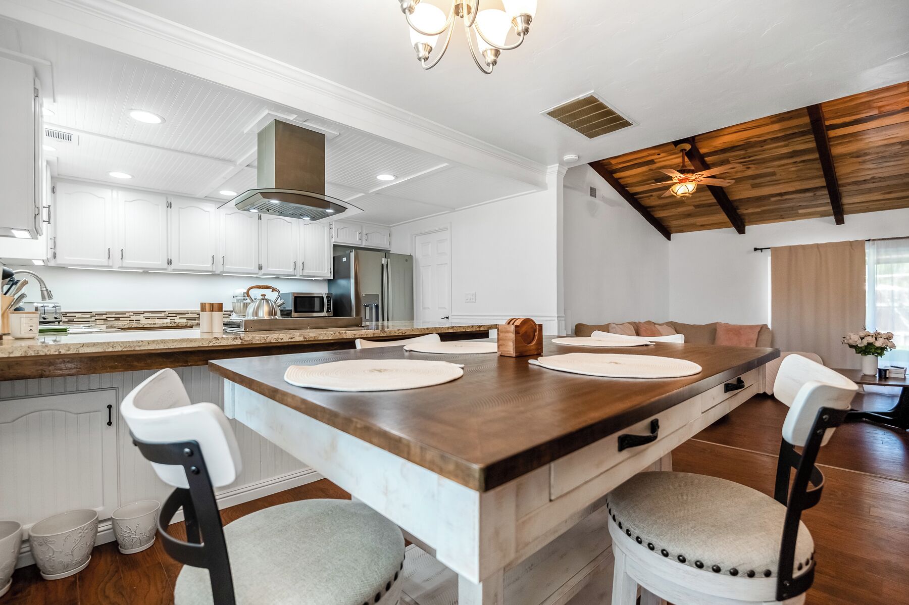 Une cuisine moderne avec des meubles blancs, un îlot central en bois doté de chaises et un ventilateur de plafond.