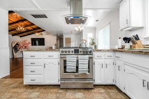 A modern kitchen with white cabinetry, a stainless steel stove, and a wooden ceiling.