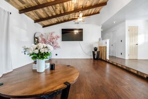 A spacious room with a wooden ceiling, a round dining table, and a flat-screen TV mounted on the wall.