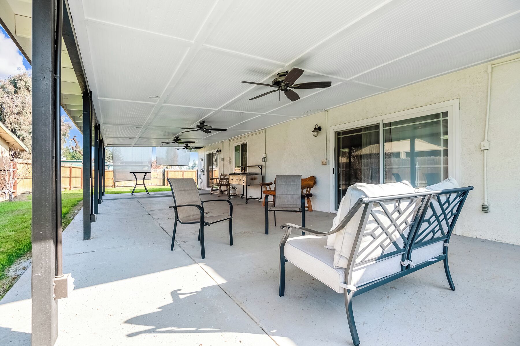 A covered patio with outdoor seating, ceiling fans, and a view of the backyard.
