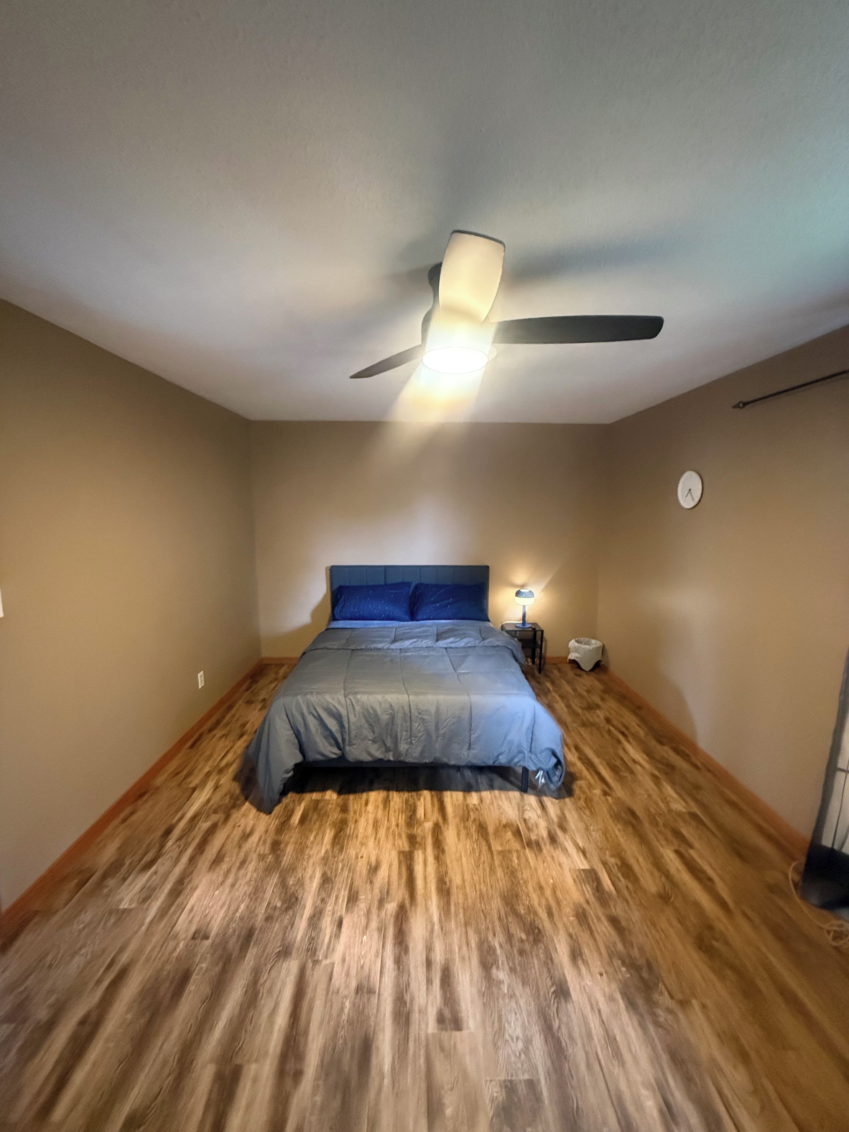 Ein Schlafzimmer mit einem Bett, einem Deckenventilator, einem Nachttisch und einer Wanduhr.