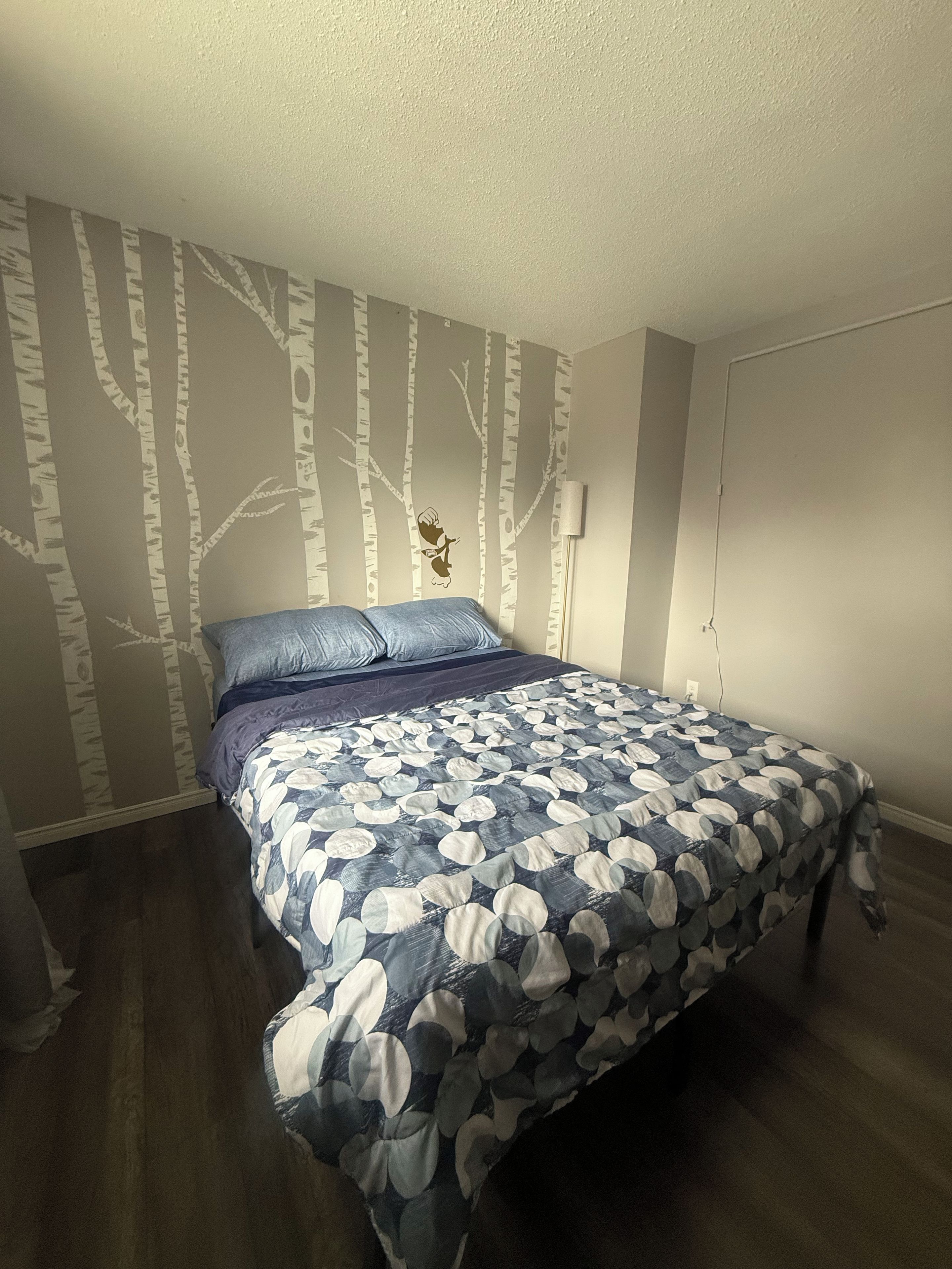 Un dormitorio con cama, pared con diseño de árbol y una puerta.