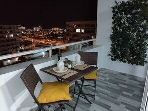 A balcony with a dining table set for two, overlooking a cityscape at night. - Blue sky:  ocean view & 5 min to Jumbo (Playa del Ingles)