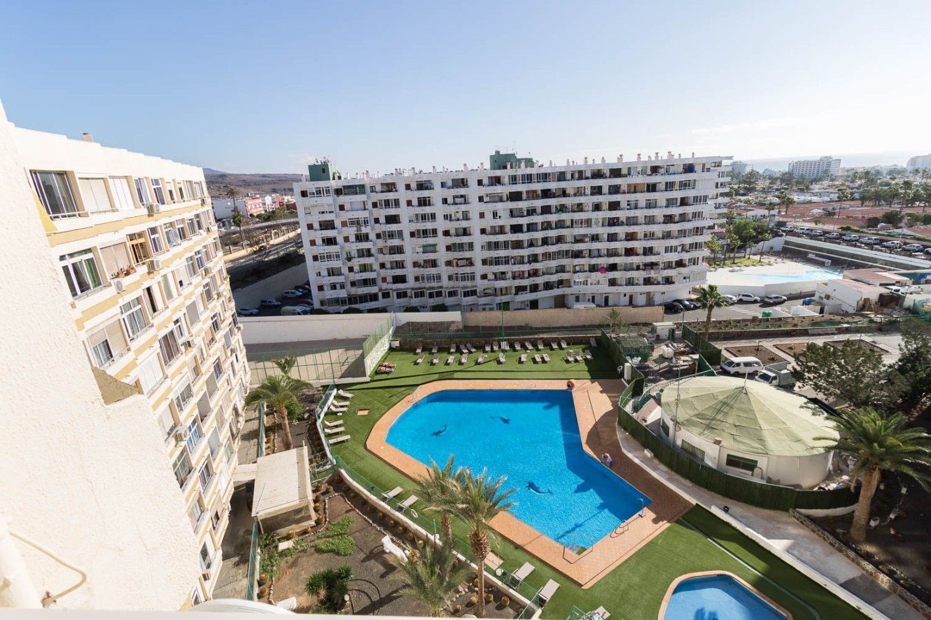 Um hotel com vários andares, piscina no terraço e vista para o mar.