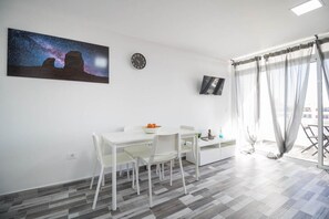 A modern room with a dining table, chairs, a painting, a clock, and a TV mounted on the wall. - Blue sky:  ocean view & 5 min to Jumbo (Playa del Ingles)