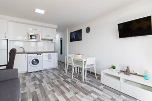 A modern kitchen with a built-in washing machine, a dining area with a table and chairs, and a flat-screen TV mounted on the wall. - Blue sky:  ocean view & 5 min to Jumbo (Playa del Ingles)