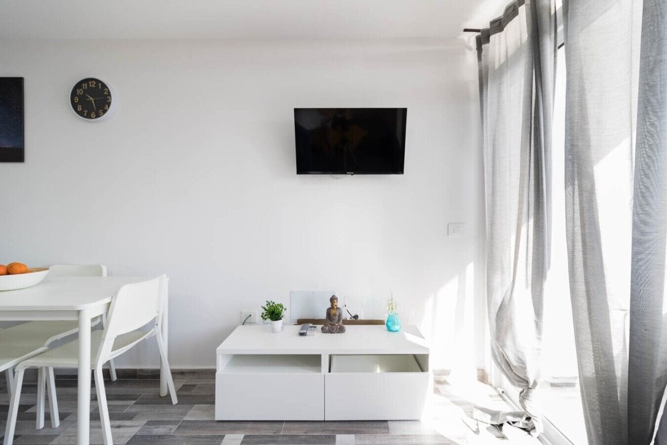Una sala de estar moderna con un sofá blanco, una mesa de centro, un televisor de pantalla plana y un reloj de pared.
