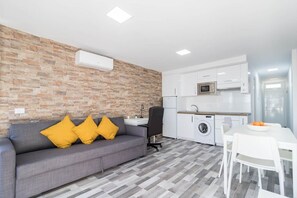 A compact living space with a grey sofa, a washing machine, and a kitchenette. - Blue sky:  ocean view & 5 min to Jumbo (Playa del Ingles)