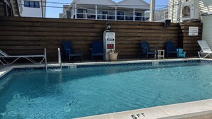 Una piscina con sillas de descanso y una cubierta de madera, rodeada por una valla.