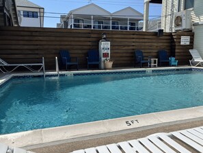 A swimming pool with lounge chairs and a wooden deck, surrounded by a fence. - Spacious 3-bedroom condo with pool and laundry, steps from beach and boardwalk! (Wildwood)