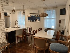 Eine moderne Küche mit Backofen, ein Essbereich mit weißem Tisch und Holzstühlen sowie eine hängende Pendelleuchte.