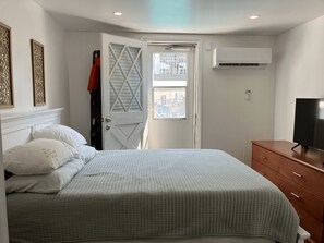 A bedroom with a bed, a wardrobe, a television, and an air conditioning unit. - Spacious 3-bedroom condo with pool and laundry, steps from beach and boardwalk! (Wildwood)