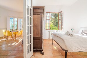 A bedroom with a bed, a window, and a dining area with chairs.
